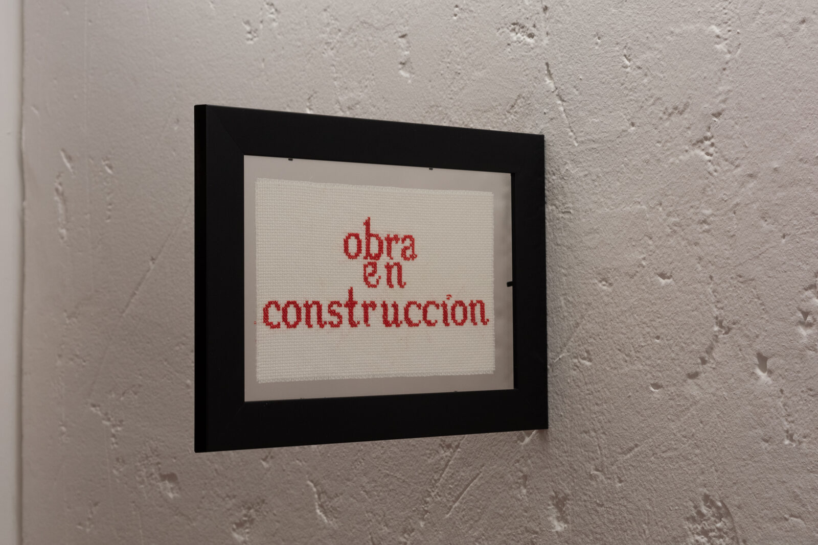 Obra en construcción — bordado en punto de cruz en rojo sobre tela cruda